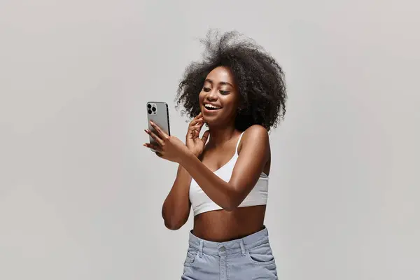 Una mujer afroamericana con estilo en una blusa blanca, sosteniendo un teléfono celular. — Stock Photo
