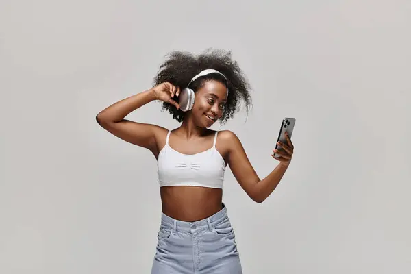 A stunning African American woman in a white top is elegantly holding a cell phone. - foto de stock