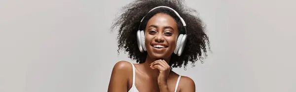 A beautiful young African American woman with curly hair wearing headphones and a white tank top. — Stock Photo