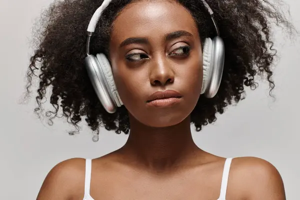 A young African American woman with curly hair listens to music through headphones. — Stock Photo