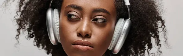 Una bella giovane donna afroamericana dai capelli ricci con le cuffie sul viso, immersa nella musica. — Foto stock