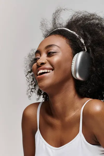 A radiant African American woman with curly hair, smiling as she listens to music through headphones. — Stock Photo