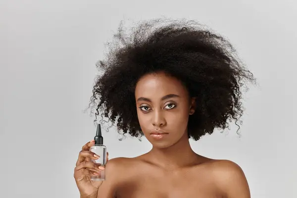 A beautiful young African American woman with curly hair holding a bottle of hair product, promoting skin care concept and self-love. — Stock Photo
