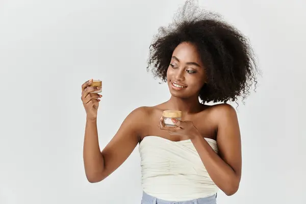 A young African American woman with curly hair holding jar with cream — Stock Photo