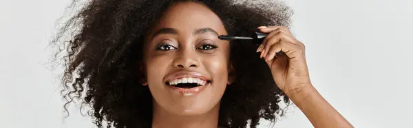 A beautiful young African American woman with curly hair applying mascara in a soothing and elegant way. — Stock Photo