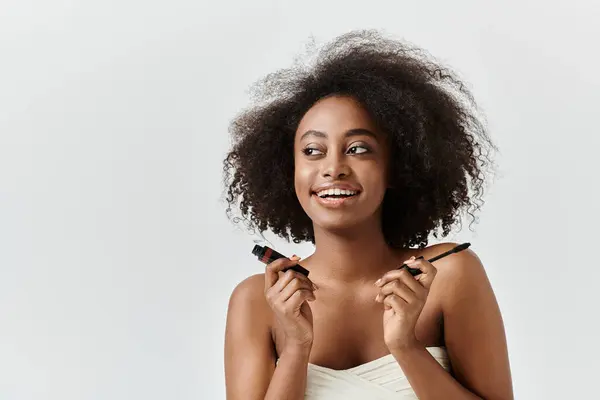 Mulher afro-americana bonita com sorrisos cabelo encaracolado enquanto segurando um rímel em um estúdio conceito cuidados da pele. — Fotografia de Stock