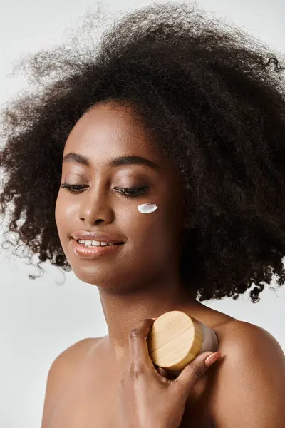 A beautiful young African American woman with curly hair and cream in a studio setting, skin care concept. — Stock Photo