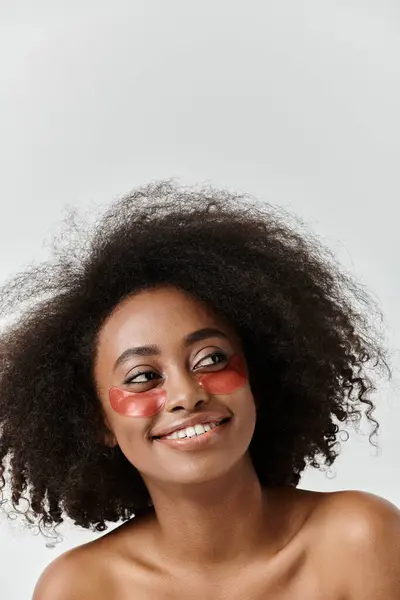 Une belle jeune femme afro-américaine aux cheveux bouclés présentant des patchs oculaires dans un cadre de studio. — Photo de stock