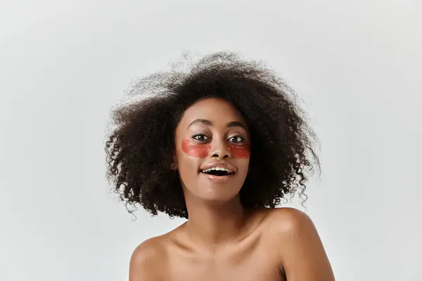 Una hermosa joven afroamericana con el pelo rizado mostrando bajo parches en los ojos, encarnando la creatividad y la auto-expresión. - foto de stock