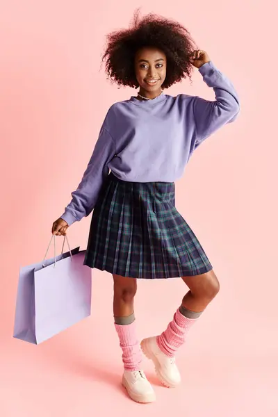 African American girl with curly hair, wearing a skirt and socks, holding a shopping bag in a fashionable studio setting. — Stock Photo