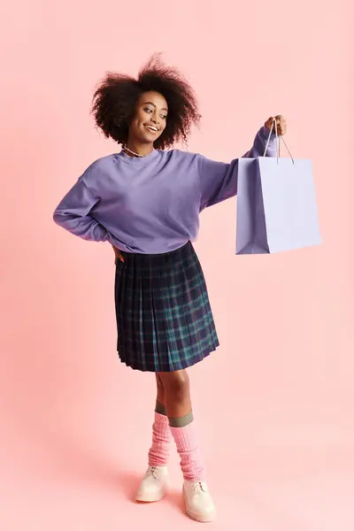 A young African American woman with curly hair smiling while holding a shopping bag. — Stock Photo