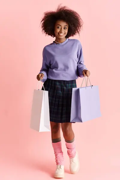 A beautiful young African American woman with curly hair holding shopping bags and smiling in a studio setting. — Stock Photo