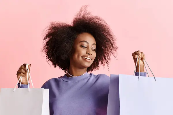 Una bella giovane donna afroamericana con i capelli ricci sta sorridendo, tenendo borse della spesa. — Foto stock