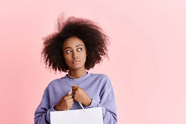 Stylish young African American lady with curly hair holding a shopping bag, showcasing fashion and glamour. — Stock Photo
