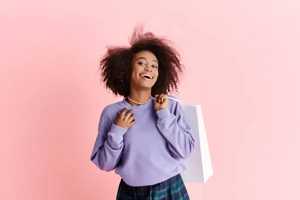A young African American woman with curly hair holding a shopping bag and smiling in a studio setting. — Stock Photo
