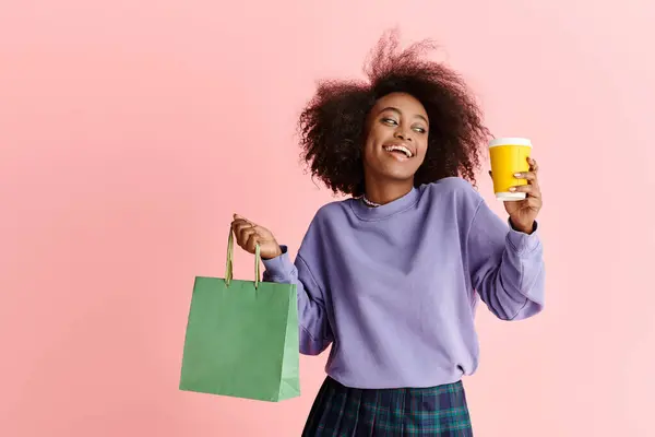 Beautiful African American woman with curly hair holding a cup of coffee and a paper bag, enjoying a morning shopping spree. — Stock Photo