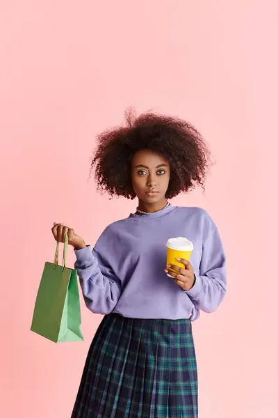 A curly-haired African American woman smiles while holding a coffee cup and paper bag. — Stock Photo