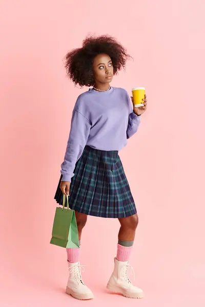 Una mujer afroamericana elegante con el pelo rizado, en una falda de moda, disfruta de una taza de café. - foto de stock