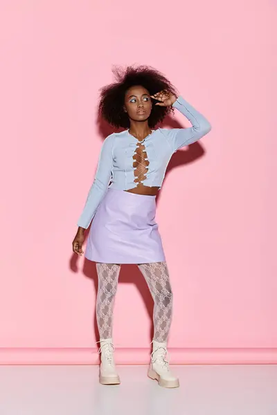 A stylish young African American woman with curly hair stands confidently in front of a bright pink wall in a studio setting. — Stock Photo
