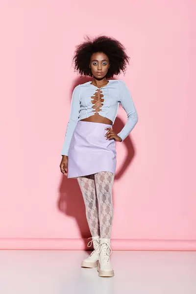 Stylish African American woman with curly hair standing confidently in front of a vibrant pink wall. — Stock Photo