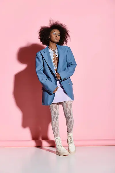 A stylish young African American woman with curly hair stands confidently in front of a vibrant pink wall. — Stock Photo