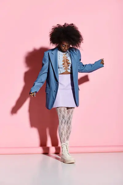 A stylish young African American woman with curly hair standing confidently in front of a vibrant pink wall. — Stock Photo