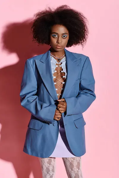StyFfsish femme afro-américaine aux cheveux bouclés posant en toute confiance dans une veste bleue et un pantalon blanc. — Photo de stock
