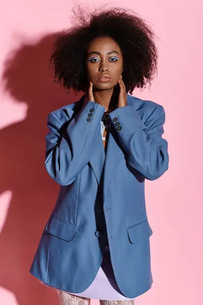 A stylish young African American woman with curly hair striking a pose in a blue blazer for a photo shoot in a studio. — Stockfoto