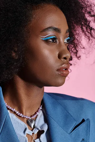 Une jeune femme afro-américaine élégante aux cheveux bouclés posant dans un costume bleu et un maquillage assorti. — Photo de stock