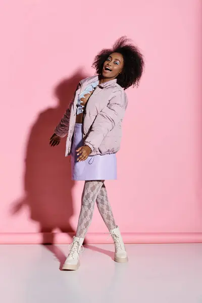 Eine elegante junge Afroamerikanerin mit lockigem Haar steht selbstbewusst vor einer lebhaften rosafarbenen Wand. — Stockfoto