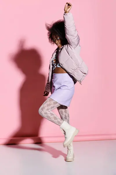 Uma jovem afro-americana com cabelo encaracolado energeticamente dançando na frente de uma parede rosa vibrante em um estúdio elegante e moderno. — Fotografia de Stock
