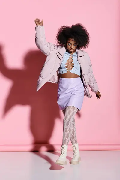 Uma jovem afro-americana com cabelo encaracolado fica confiante na frente de uma parede rosa vibrante, apresentando sua saia elegante e conjunto de jaquetas. — Fotografia de Stock