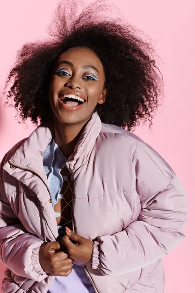 A stylish young African American woman with curly hair wearing a jacket and a blue makeup poses confidently in a studio. — Stock Photo