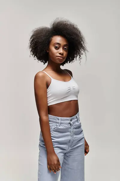 Uma mulher afro-americana elegante com cabelo encaracolado vestindo um top de cultura e jeans. — Fotografia de Stock