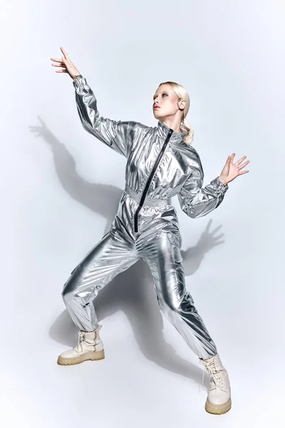 Extravagante Frau in silberner futuristischer Kleidung posiert in Bewegung vor grauem Hintergrund und schaut weg — Stockfoto