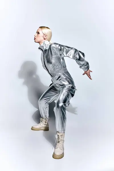 Schöne Frau in silberfarbener futuristischer Kleidung posiert in Bewegung vor grauem Hintergrund und schaut weg — Stockfoto