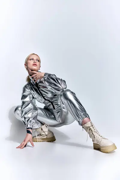 Hermosa mujer en traje futurista plateado posando en movimiento sobre fondo gris y mirando hacia otro lado - foto de stock