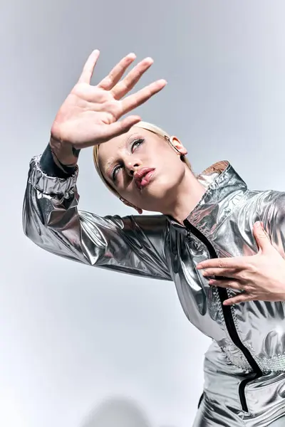 Gut aussehende Frau in silberner futuristischer Kleidung posiert in Bewegung vor grauem Hintergrund und schaut weg — Stockfoto
