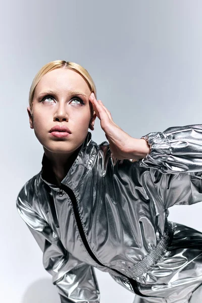 Mujer futurista en traje inusual de plata posando en movimiento sobre fondo gris y mirando hacia otro lado - foto de stock