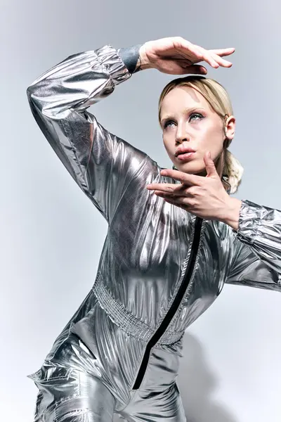 Futuristische Frau in silberner, ungewöhnlicher Kleidung posiert in Bewegung vor grauem Hintergrund und schaut weg — Stockfoto