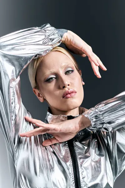 Donna attraente con i capelli biondi in futuristico abbigliamento argento in posa in movimento su sfondo grigio — Foto stock