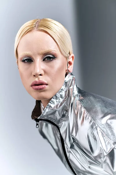 Mulher atraente com cabelo loiro em trajes de prata futurista posando em movimento no fundo cinza — Fotografia de Stock