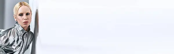 Donna chic con i capelli biondi in futuristico abbigliamento argento in posa in movimento su sfondo grigio, banner — Foto stock