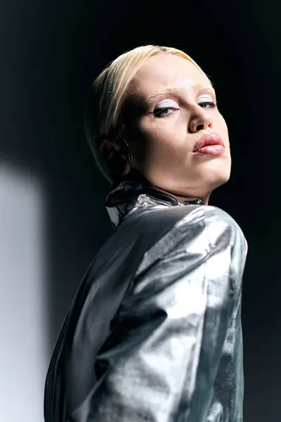 Extraordinaria mujer con el pelo rubio en traje de plata futurista posando en movimiento sobre fondo gris - foto de stock