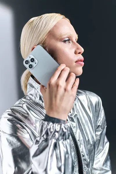 Mulher loira de boa aparência com maquiagem em trajes robóticos prata falando por telefone e olhando para longe — Fotografia de Stock