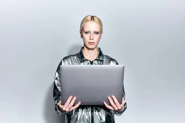 Beautiful blonde female model in robotic silver outfit holding laptop and looking at camera — Stock Photo