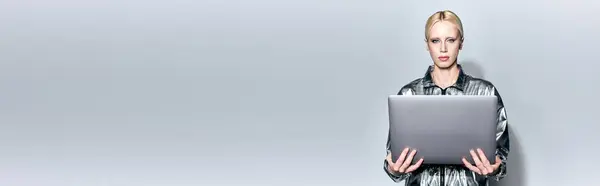 Modelo feminino loira bonita em roupa de prata robótica segurando laptop e olhando para a câmera, banner — Fotografia de Stock