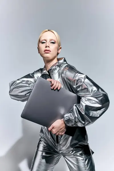Beautiful blonde female model in robotic silver outfit holding laptop and looking at camera — Stock Photo