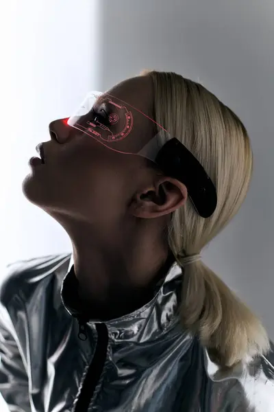 Красивая женщина в футуристических очках в роботизированном серебристом одеянии смотрит в сторону на сером фоне — стоковое фото