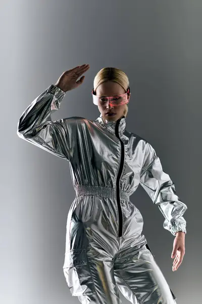 Mulher extraordinária com óculos futuristas em traje de prata fazendo movimentos robóticos e olhando para longe — Fotografia de Stock